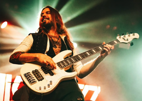 Eric Juris smiling while playing 5-string bass live on tour with Alcatrazz